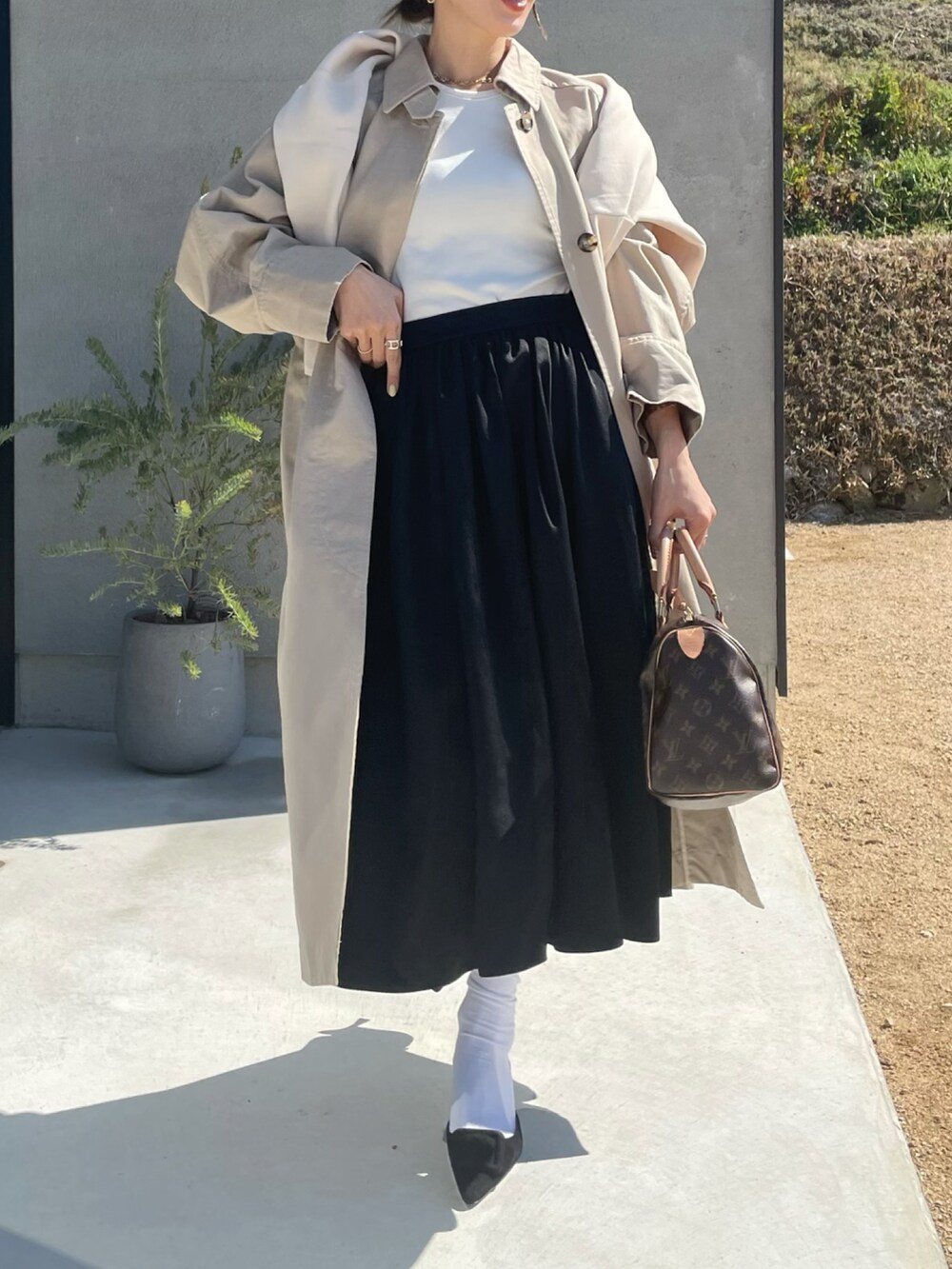 ベージュ系のその他アウター、ホワイト系のニット/セーター、ブラック系のスカートを着用したレディースの春コーディネートの2枚目の写真