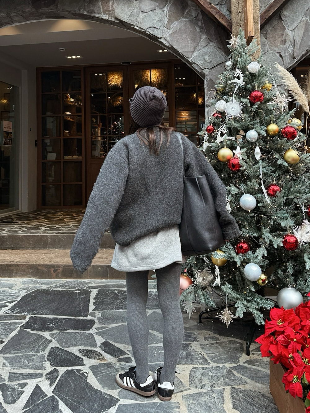 グレー系のニット/セーター、グレー系のスカート、ブラック系のスニーカーを着用したレディースの秋コーディネートの2枚目の写真