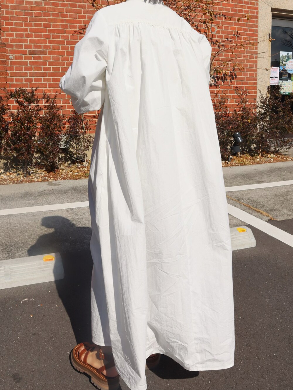 ホワイト系のシャツワンピース、ゴールド系のエコバッグ/サブバッグ、ブラウン系のサンダルを着用したレディースの冬コーディネートの2枚目の写真