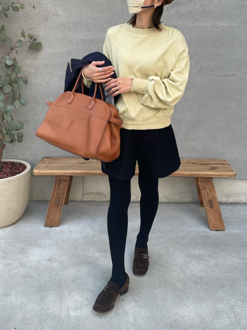 イエロー系のスウェット、ブラウン系のハンドバッグ、ブラウン系のハンチング/ベレー帽を着用したレディースの冬コーディネートの2枚目の写真