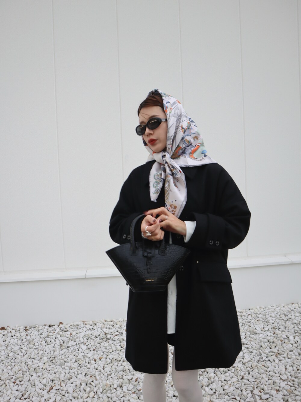 ブラック系のショルダーバッグ、ブラック系のステンカラーコート、ブラック系のローファーを着用したレディースの冬コーディネートの2枚目の写真