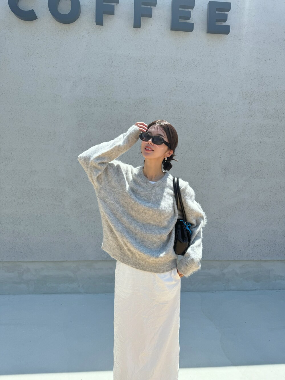 グレー系のニット/セーター、ホワイト系のスカート、ブラック系のボストンバッグを着用したレディースの夏コーディネートの2枚目の写真