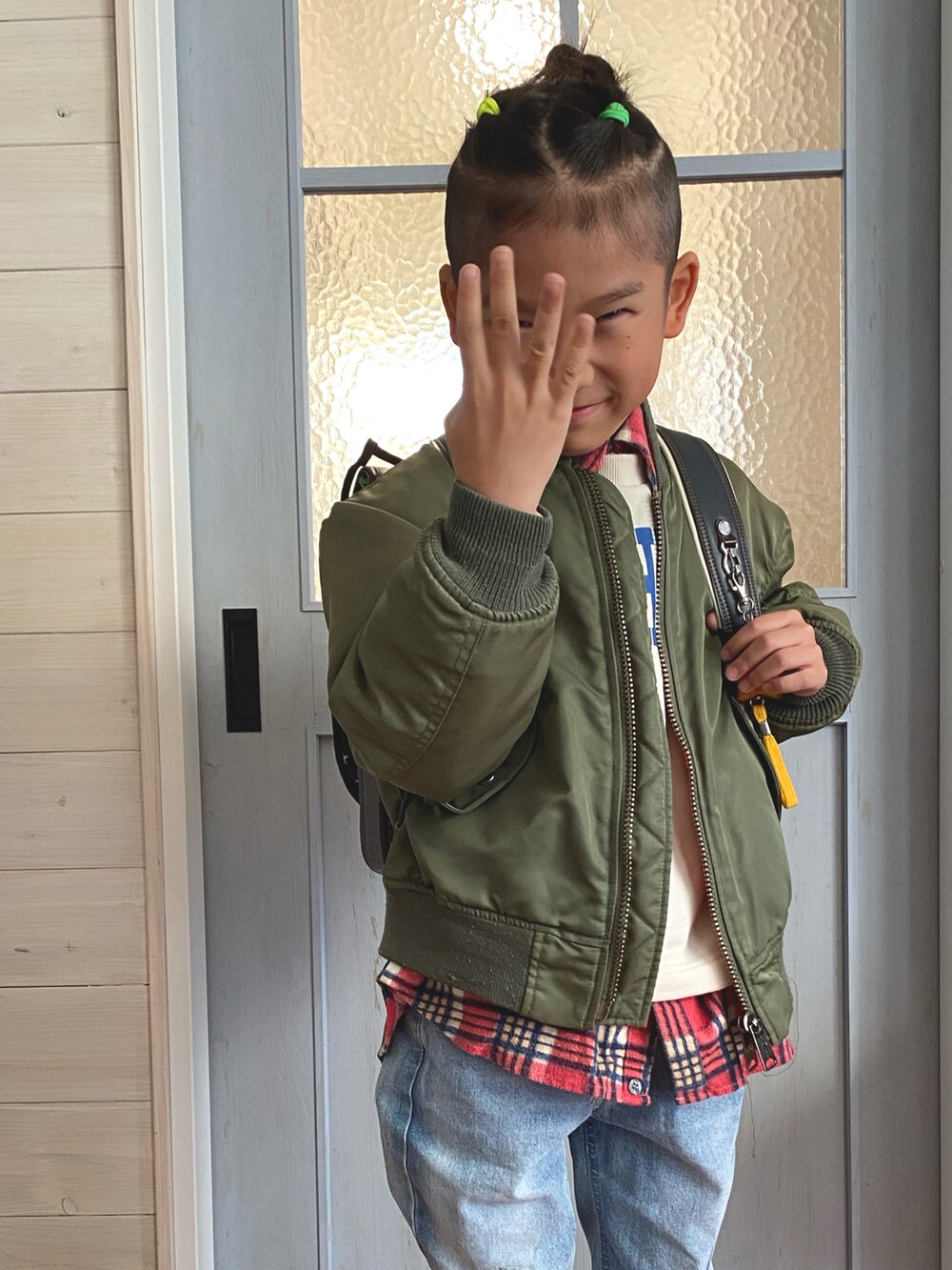 グリーン系のミリタリージャケット、ブルー系のデニムパンツ、ブラック系のスニーカーを着用したキッズの秋コーディネートの2枚目の写真