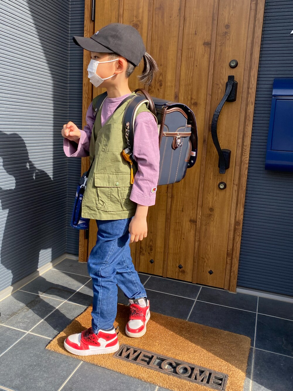 グリーン系のベスト、レッド系のスニーカー、ブルー系のランドセルを着用したキッズの春コーディネートの2枚目の写真