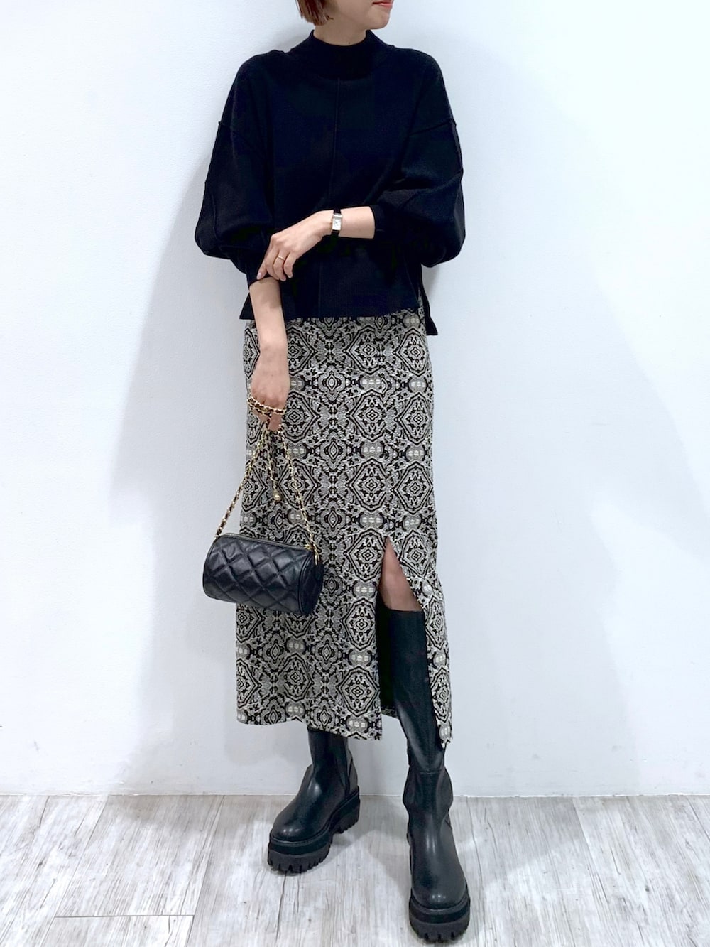 ブラック系のショルダーバッグ、ブラック系のブーツ、ブラック系のスカートを着用したレディースの秋コーディネートの2枚目の写真