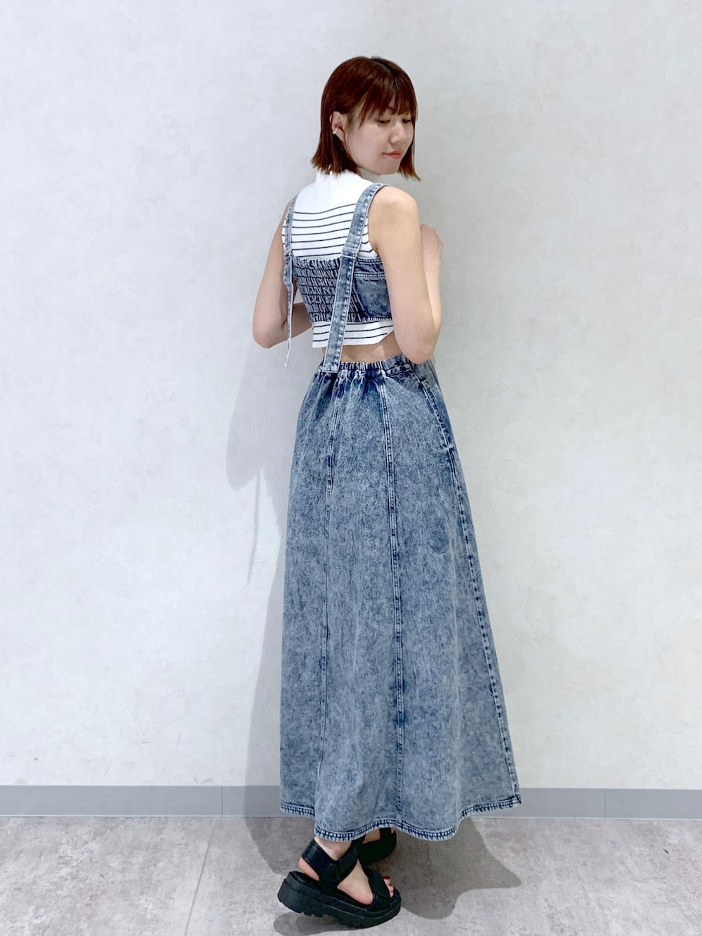 ブルー系のジャンパースカート、ブラック系のサンダル、オレンジ系のショルダーバッグを着用したレディースの夏コーディネートの3枚目の写真