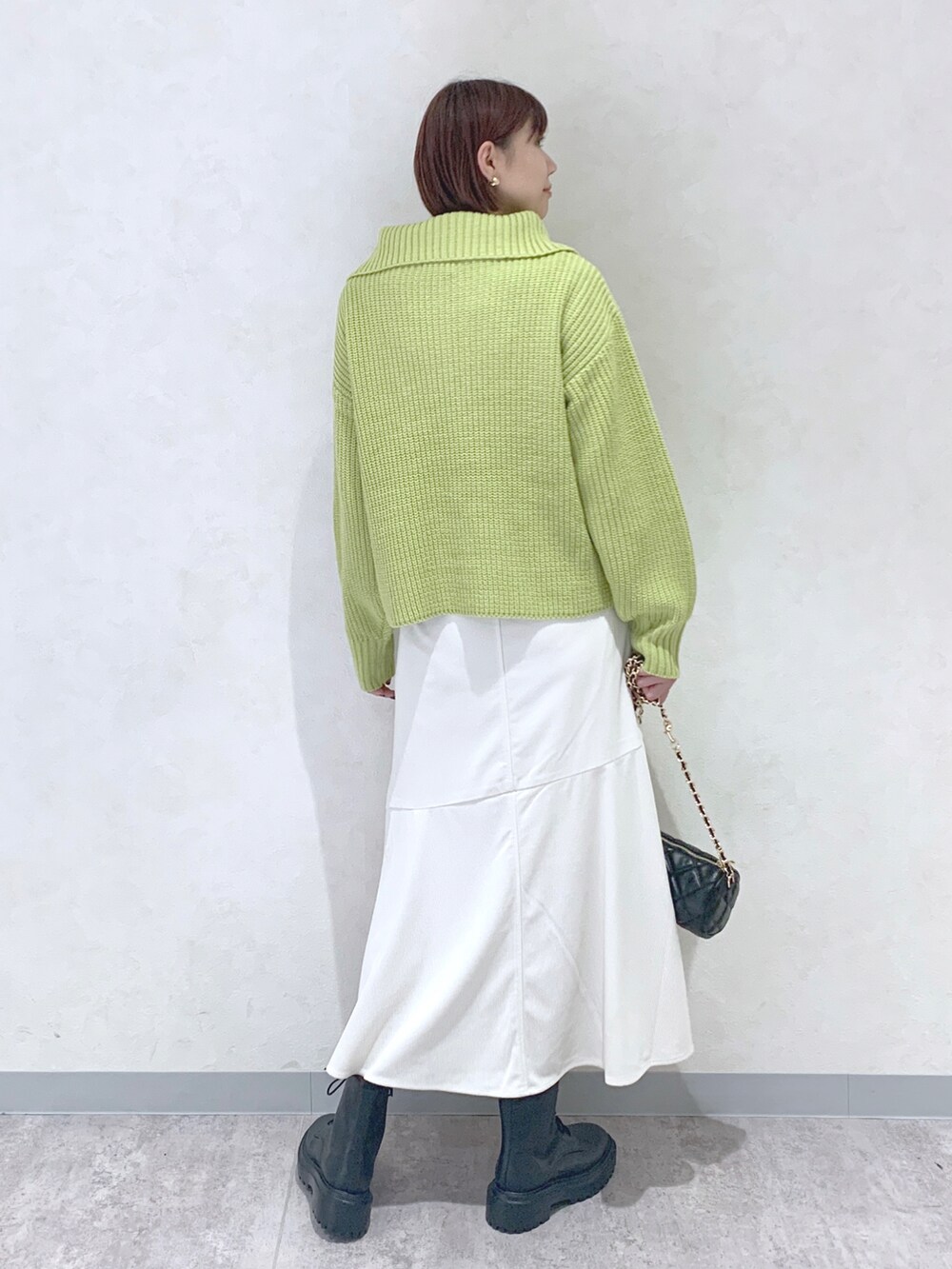 イエロー系のニット/セーター、ホワイト系のスカート、ブラック系のブーツを着用したレディースの秋コーディネートの4枚目の写真