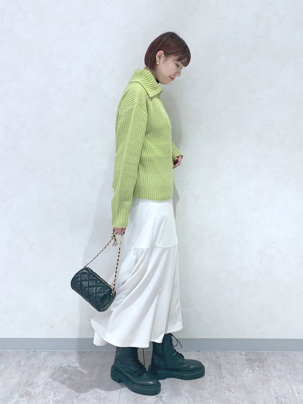 イエロー系のニット/セーター、ホワイト系のスカート、ブラック系のブーツを着用したレディースの秋コーディネートの3枚目の写真
