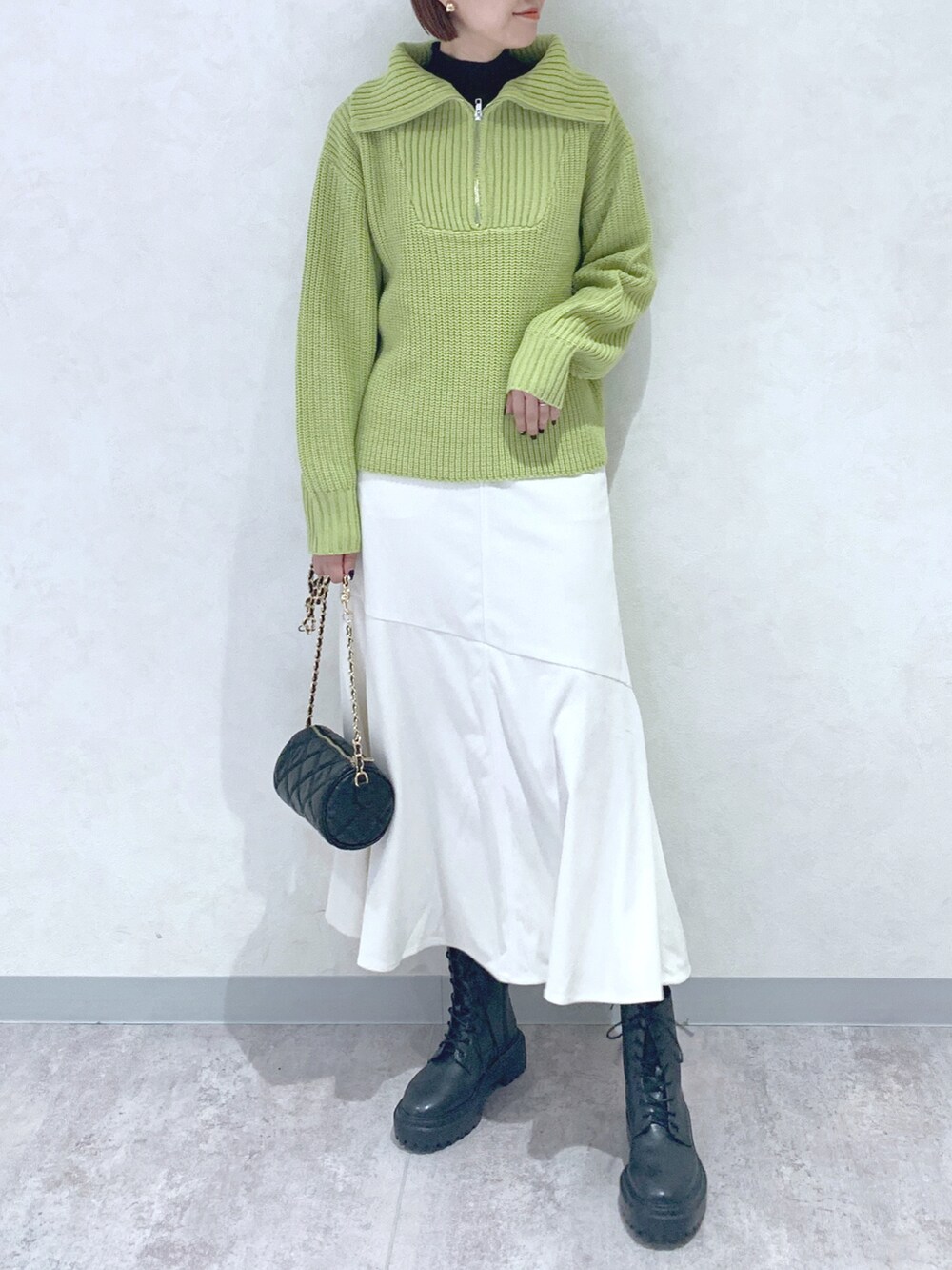 イエロー系のニット/セーター、ホワイト系のスカート、ブラック系のブーツを着用したレディースの秋コーディネートの2枚目の写真