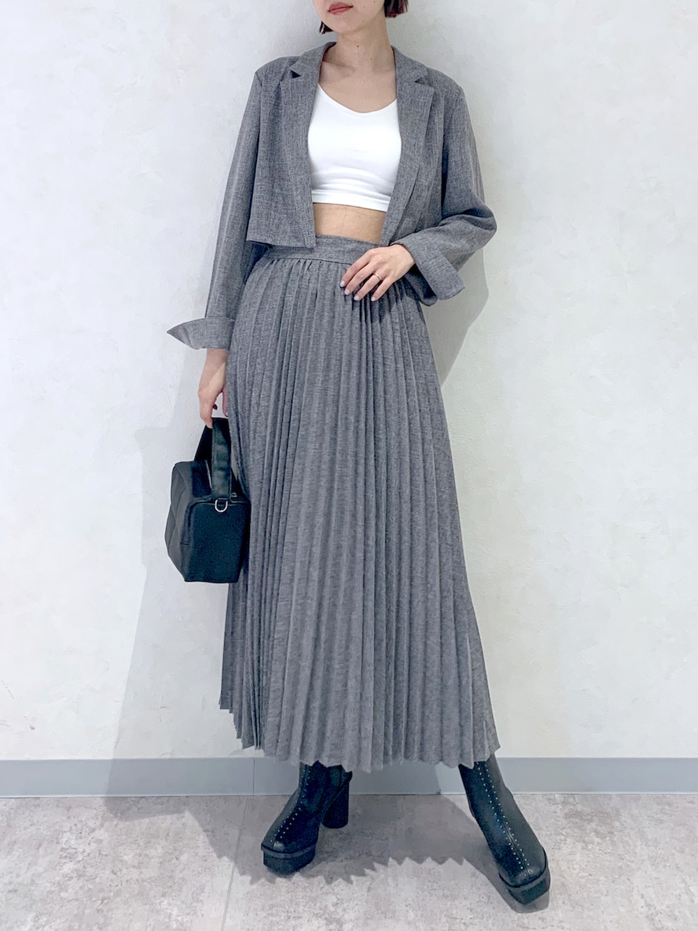 グレー系のスカート、ブラック系のショルダーバッグ、ブラック系のブーツを着用したレディースの夏コーディネートの2枚目の写真