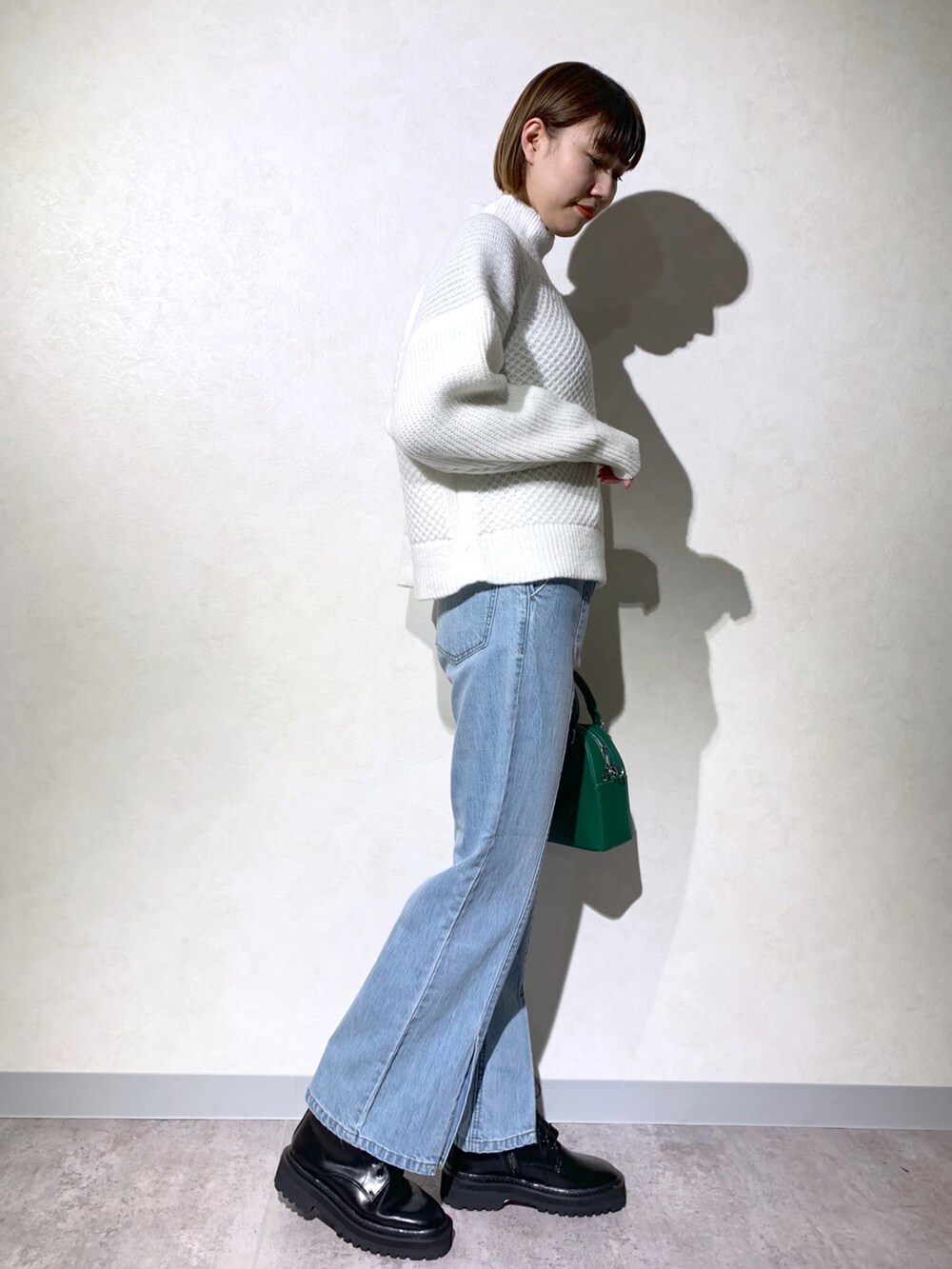 グリーン系のショルダーバッグ、ホワイト系のニット/セーター、ブルー系のデニムパンツを着用したレディースの冬コーディネートの2枚目の写真
