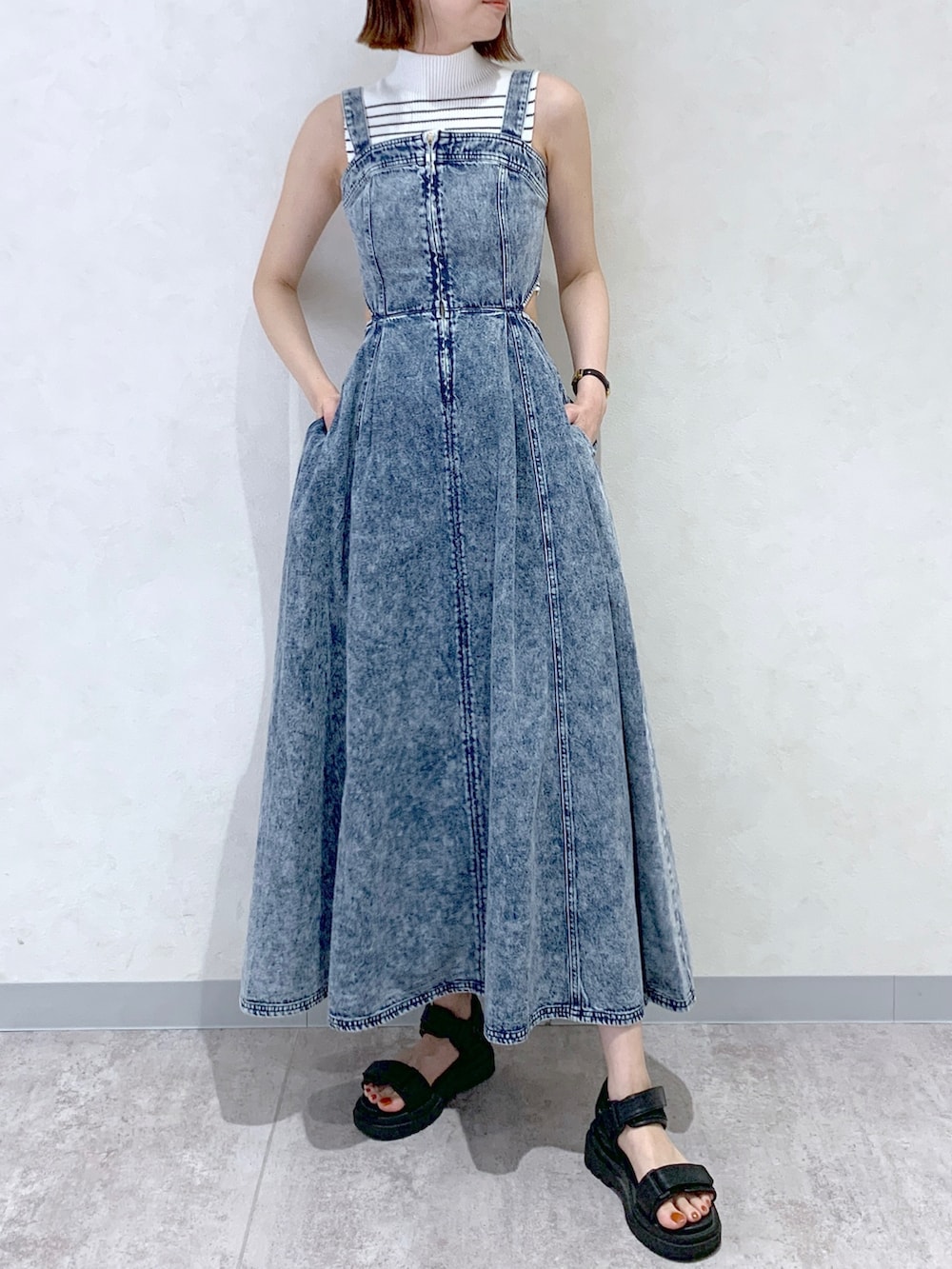 ブルー系のジャンパースカート、ブラック系のサンダル、オレンジ系のショルダーバッグを着用したレディースの夏コーディネートの2枚目の写真