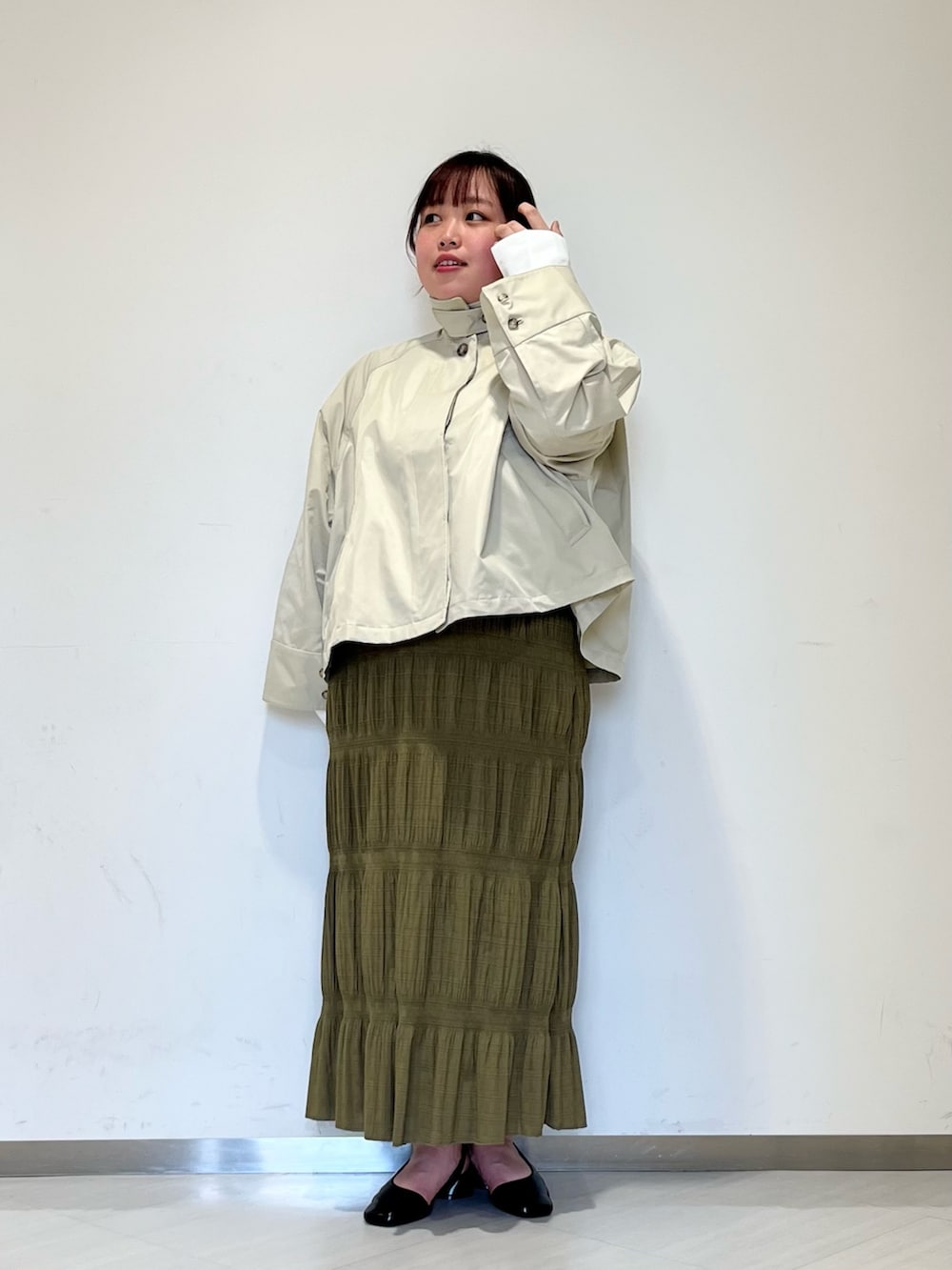 グレー系のステンカラーコート、グリーン系のセットアップ、ブラック系のパンプスを着用したレディースの冬コーディネートの3枚目の写真