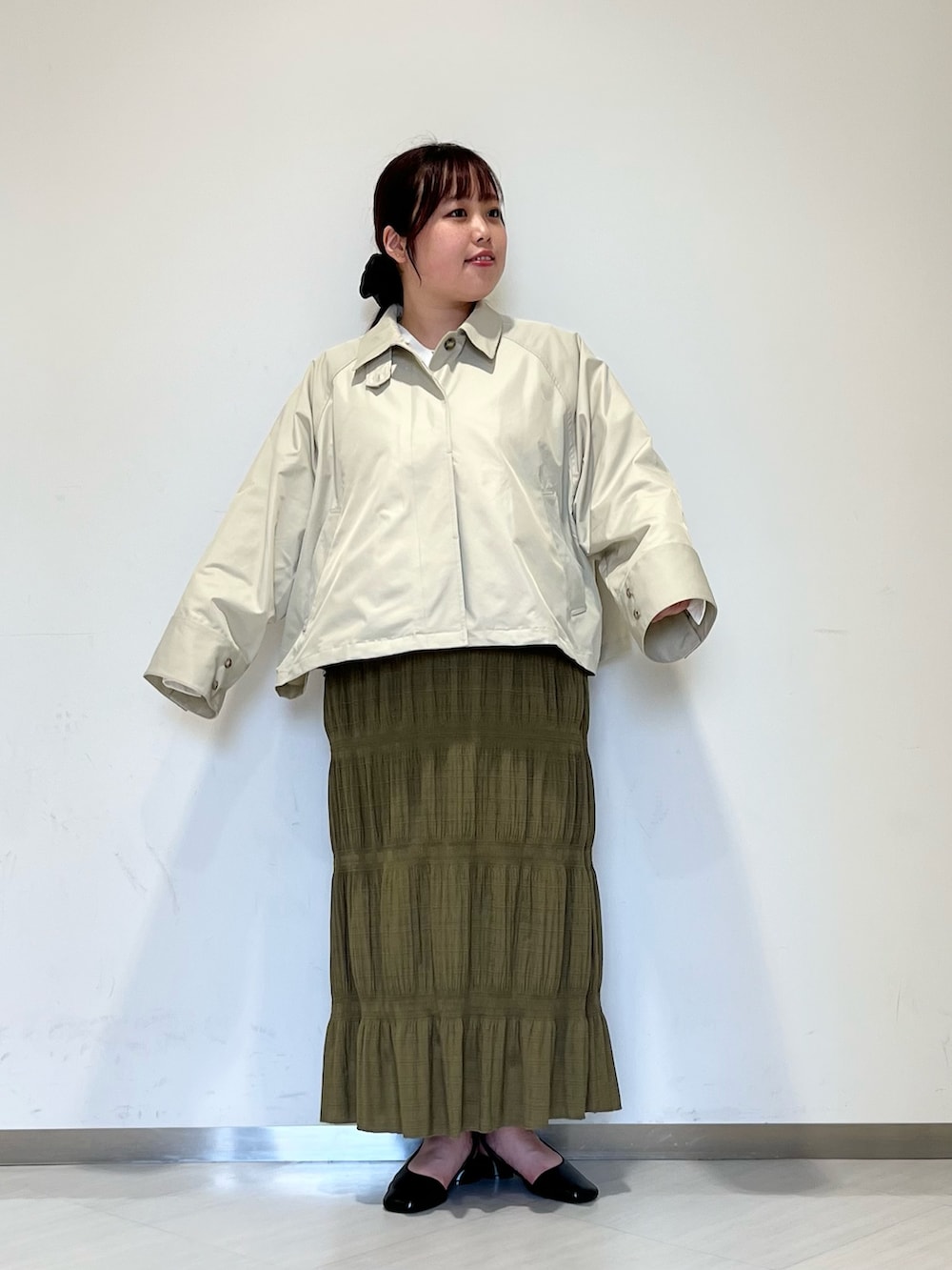 グレー系のステンカラーコート、グリーン系のセットアップ、ブラック系のパンプスを着用したレディースの冬コーディネートの2枚目の写真