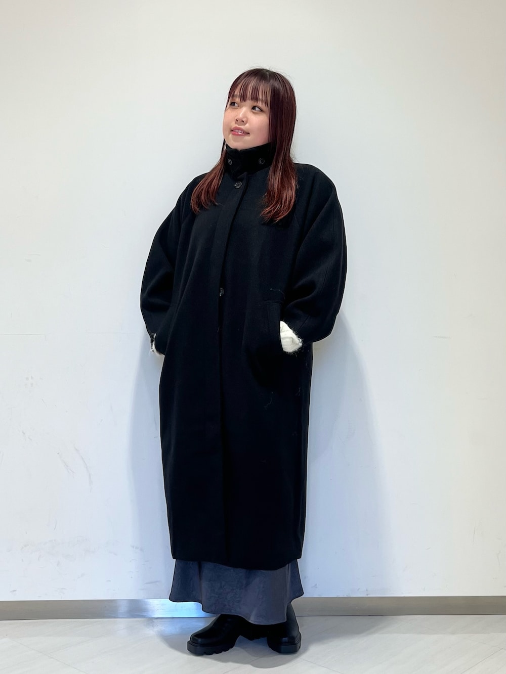 ブラック系のステンカラーコート、ホワイト系のニット/セーター、グレー系のスカートを着用したレディースの冬コーディネートの2枚目の写真