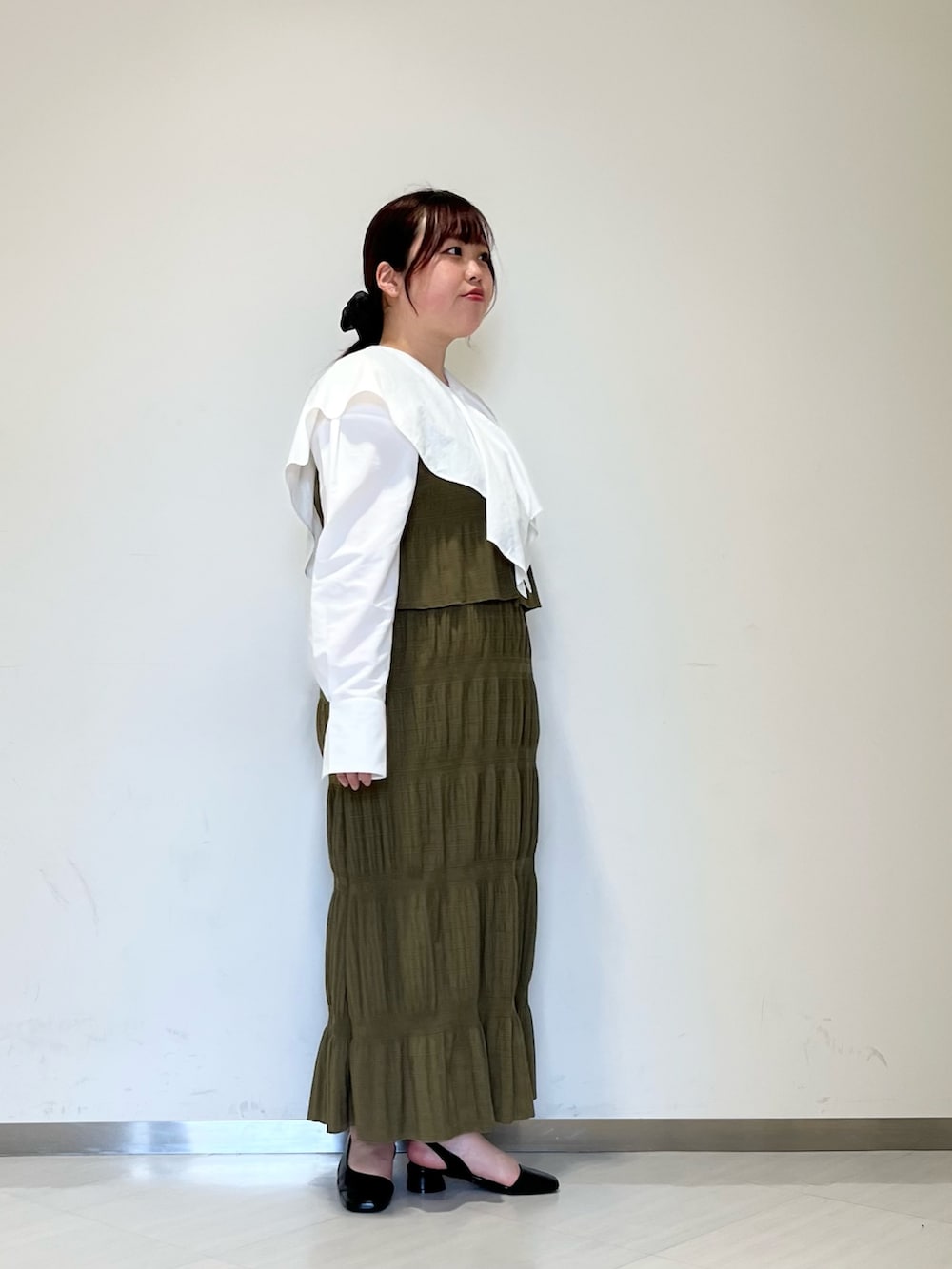 グレー系のステンカラーコート、グリーン系のセットアップ、ブラック系のパンプスを着用したレディースの冬コーディネートの6枚目の写真