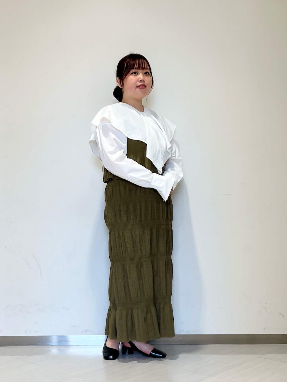 グレー系のステンカラーコート、グリーン系のセットアップ、ブラック系のパンプスを着用したレディースの冬コーディネートの4枚目の写真