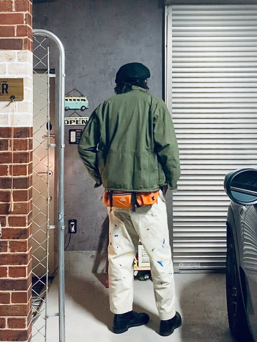 グリーン系のミリタリージャケット、ブラック系のブーツ、オレンジ系のボディバッグ/ウエストポーチを着用したメンズの秋コーディネートの2枚目の写真