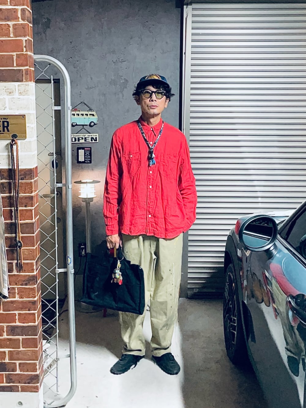 レッド系のシャツ/ブラウス、ベージュ系のチノパンツ、ブラック系のトートバッグを着用したメンズの秋コーディネートの2枚目の写真