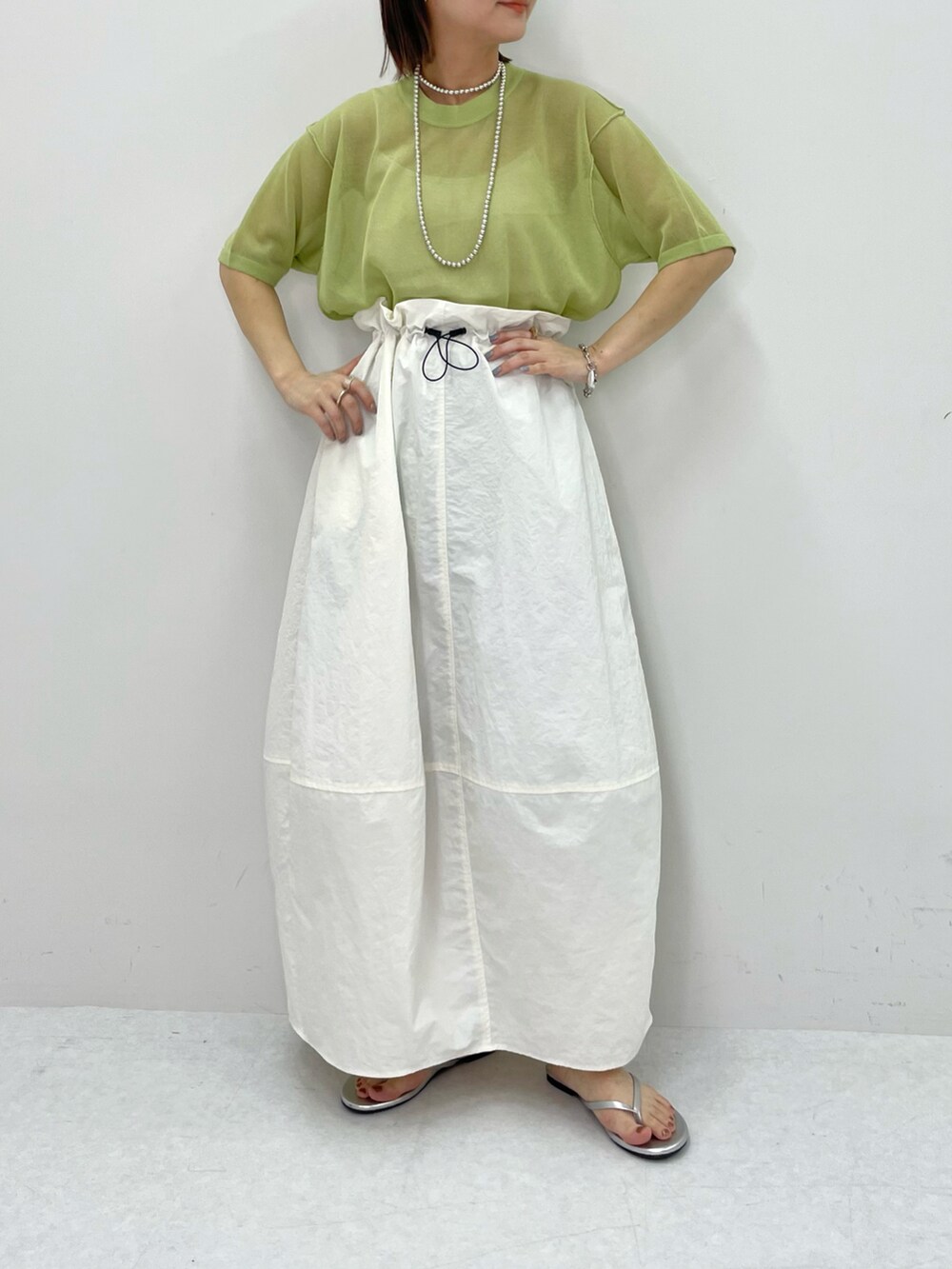 ホワイト系のスカート、グリーン系のニット/セーター、シルバー系のネックレスを着用したレディースの春コーディネートの2枚目の写真