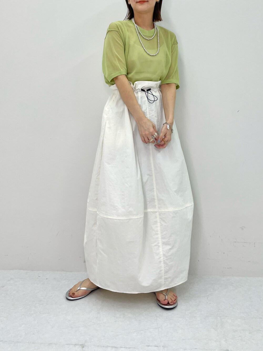 ホワイト系のスカート、グリーン系のニット/セーター、シルバー系のネックレスを着用したレディースの春コーディネートの3枚目の写真