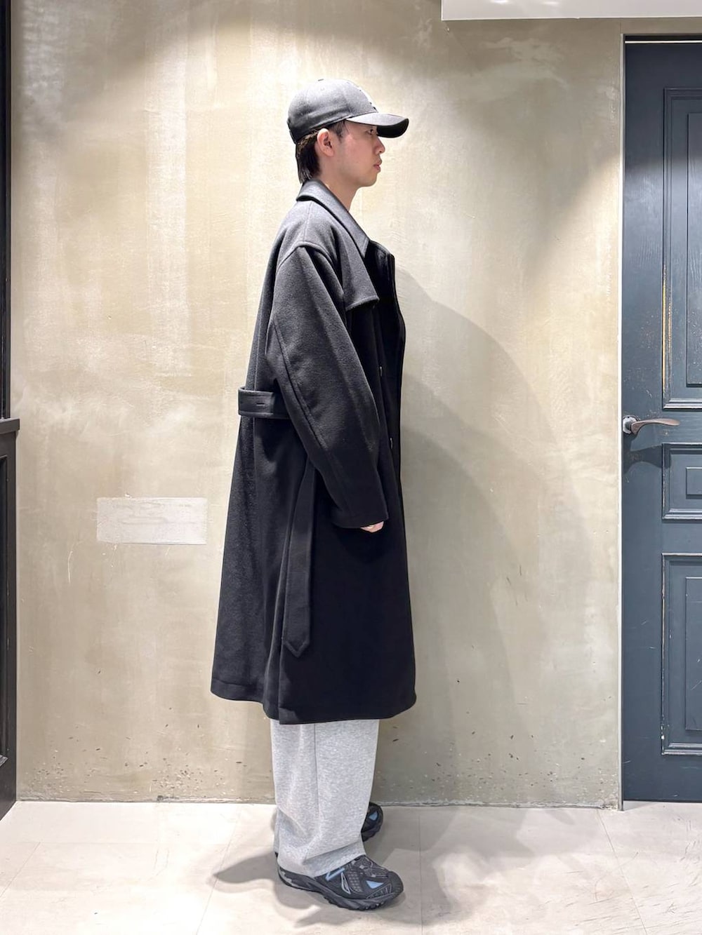 ブラック系のトレンチコート、グレー系のスウェットパンツ、ブラック系のニット/セーターを着用したメンズの冬コーディネートの2枚目の写真