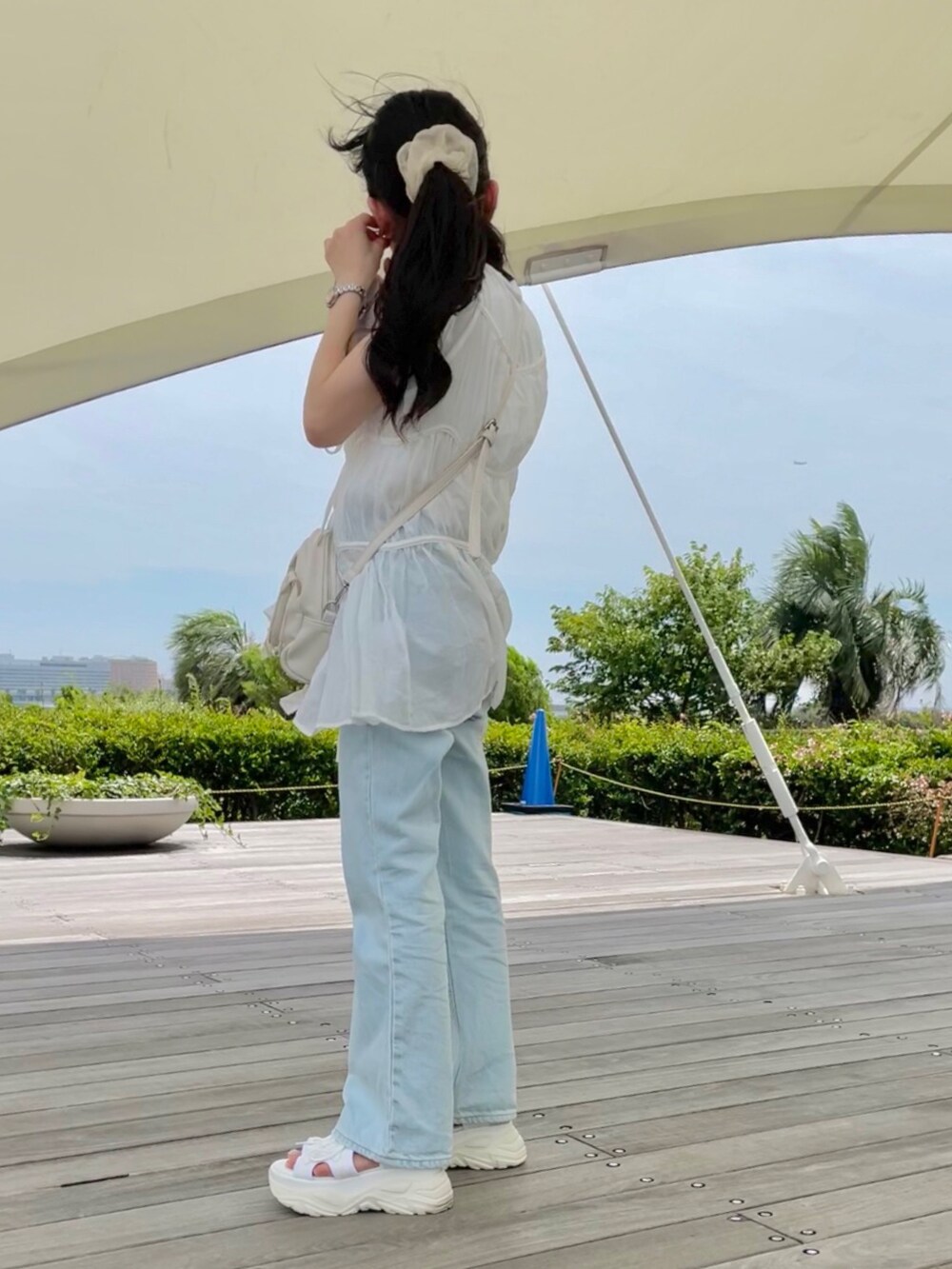 ブルー系のデニムパンツ、ホワイト系のサンダル、ホワイト系のショルダーバッグを着用したレディースの夏コーディネートの2枚目の写真