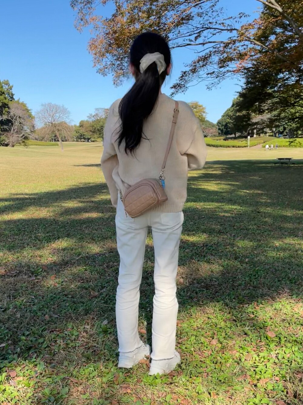 ベージュ系のショルダーバッグ、ホワイト系のデニムパンツ、ホワイト系のスニーカーを着用したレディースの秋コーディネートの2枚目の写真