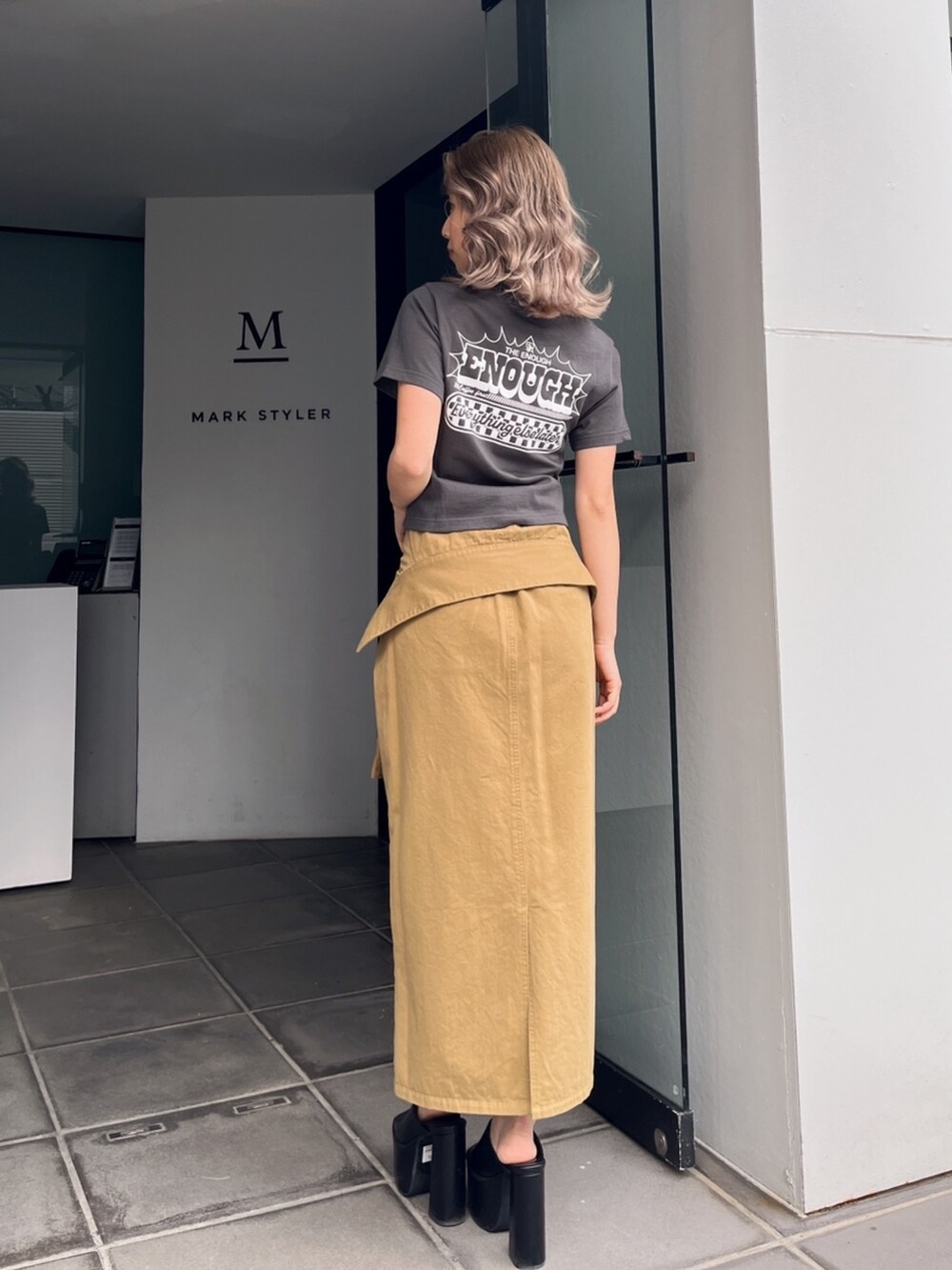 グレー系のTシャツ/カットソー、グリーン系のスカート、ブラック系のサンダルを着用したレディースの秋コーディネートの3枚目の写真