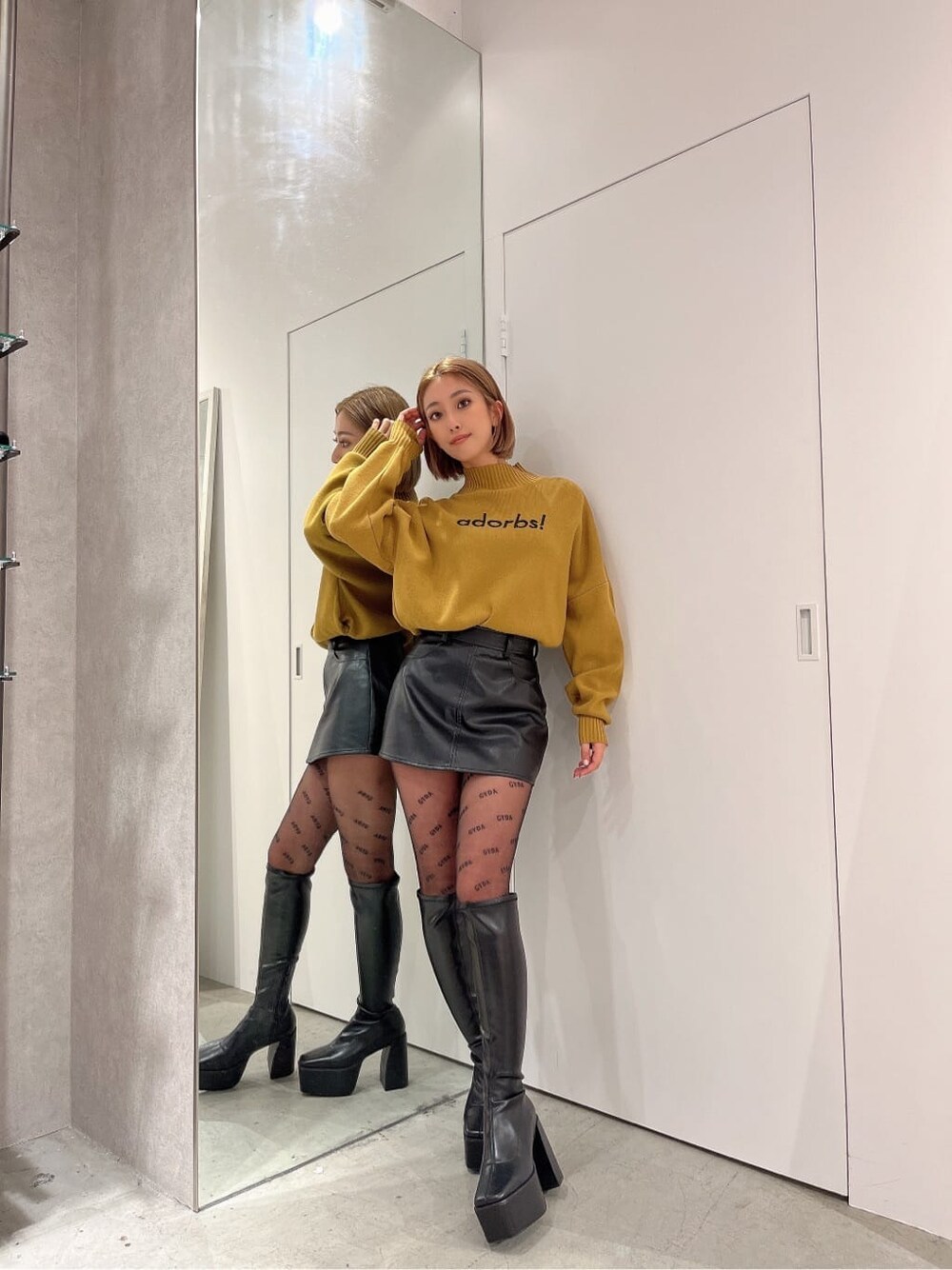 ブラック系のブーツ、イエロー系のニット/セーター、ブラック系のスカートを着用したレディースの秋コーディネートの2枚目の写真