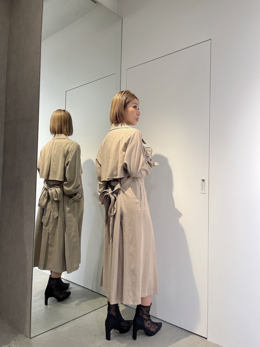 ブラック系のワンピース、ホワイト系のトレンチコート、ブラック系のブーツを着用したレディースの春コーディネートの3枚目の写真