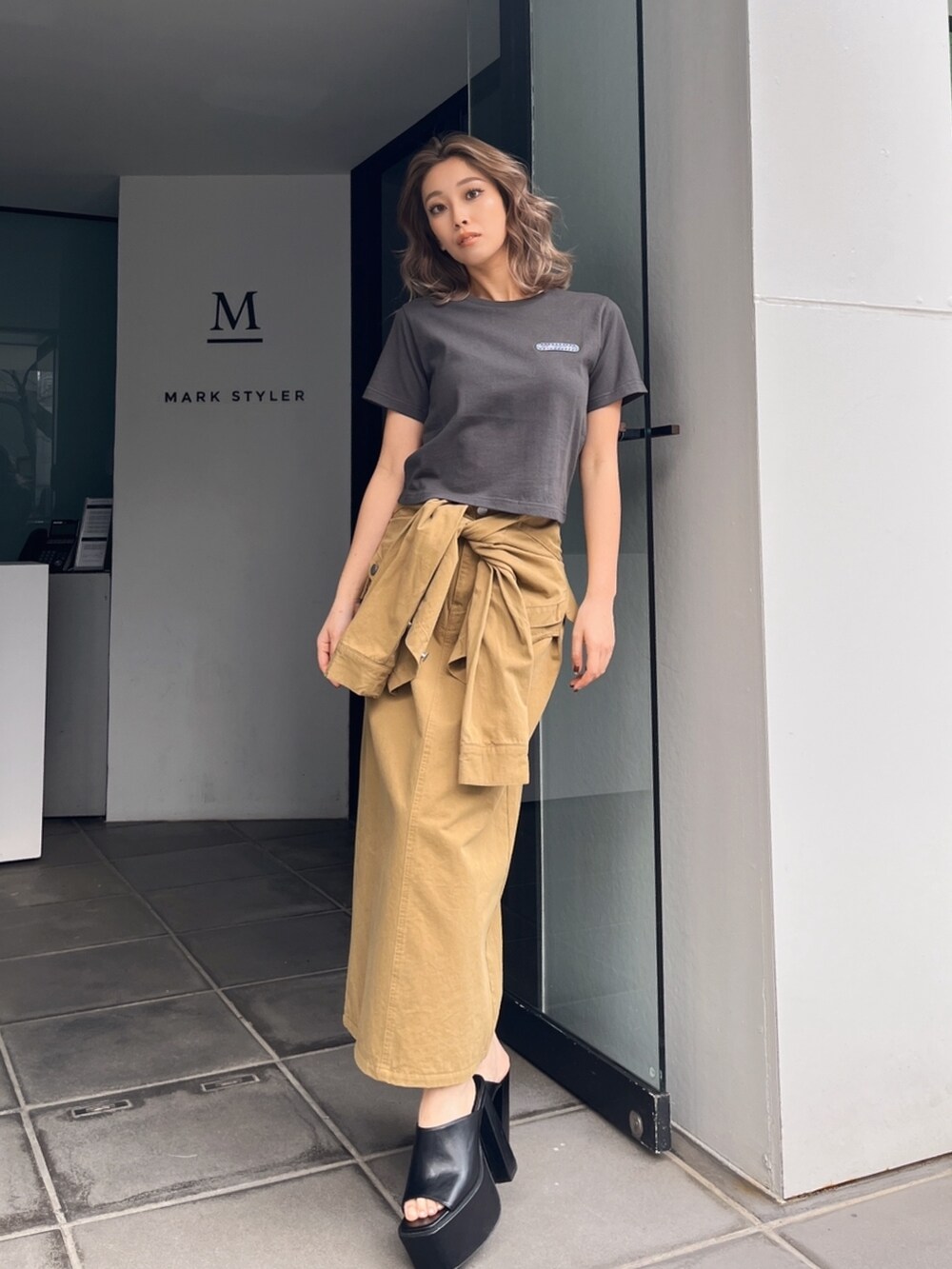 グレー系のTシャツ/カットソー、グリーン系のスカート、ブラック系のサンダルを着用したレディースの秋コーディネートの2枚目の写真