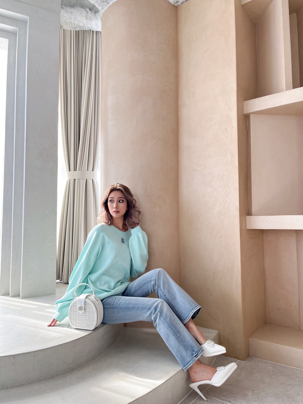 グリーン系のニット/セーター、ブルー系のデニムパンツ、ホワイト系のハンドバッグを着用したレディースの冬コーディネートの2枚目の写真