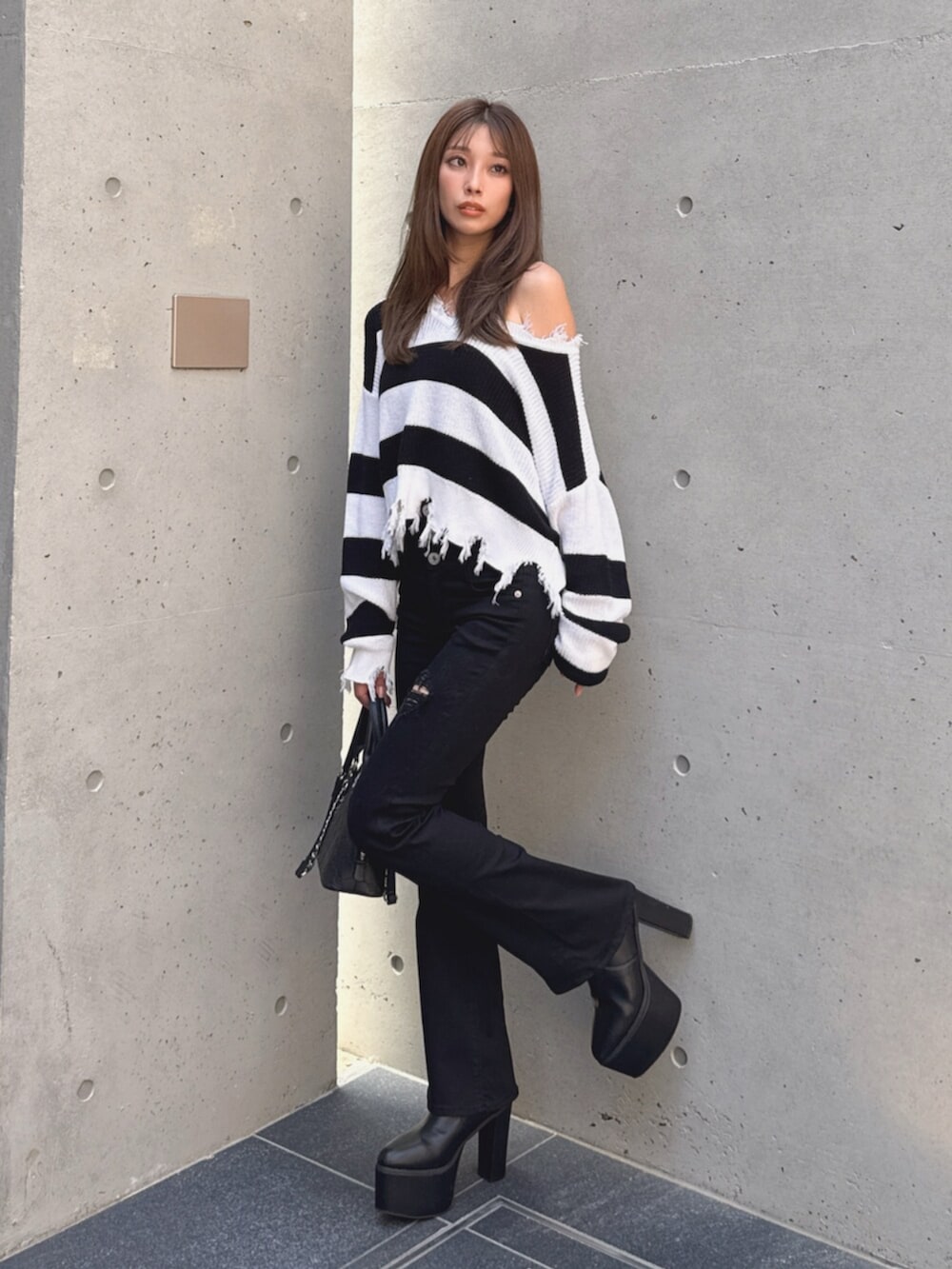 ブラック系のデニムパンツ、ブラック系のブーツ、ホワイト系のハンドバッグを着用したレディースの秋コーディネートの2枚目の写真