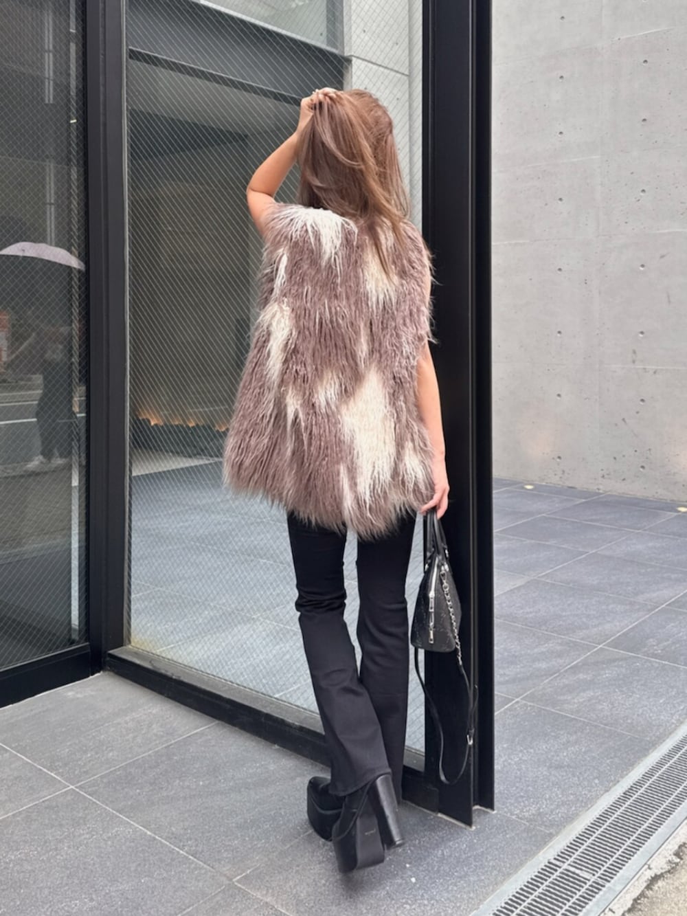 ブラック系のデニムパンツ、ブラック系のブーツ、ホワイト系のハンドバッグを着用したレディースの秋コーディネートの3枚目の写真