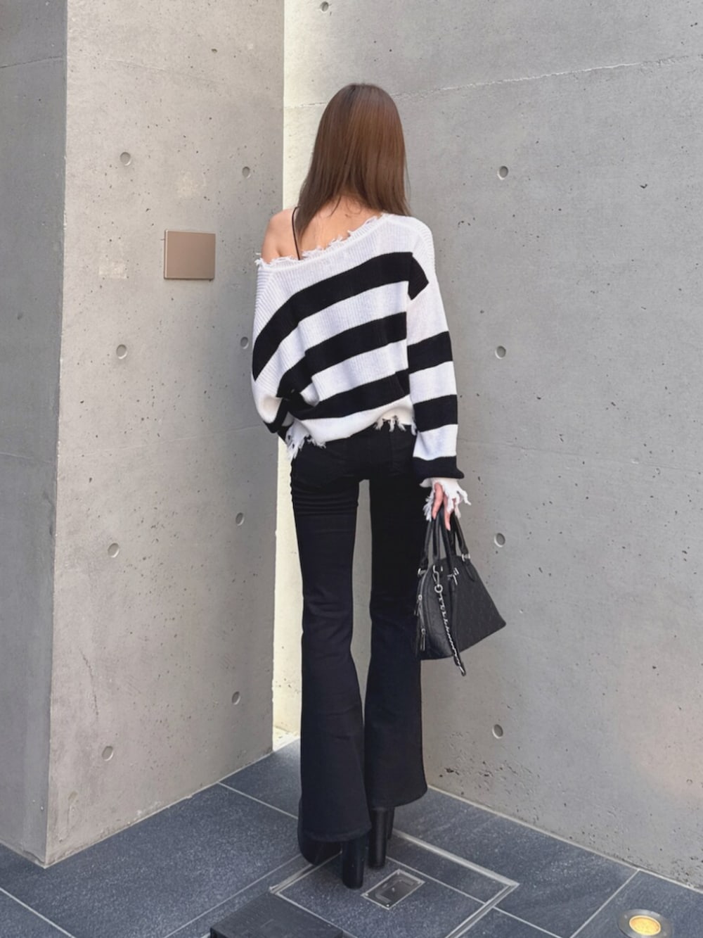 ブラック系のデニムパンツ、ブラック系のブーツ、ホワイト系のハンドバッグを着用したレディースの秋コーディネートの3枚目の写真