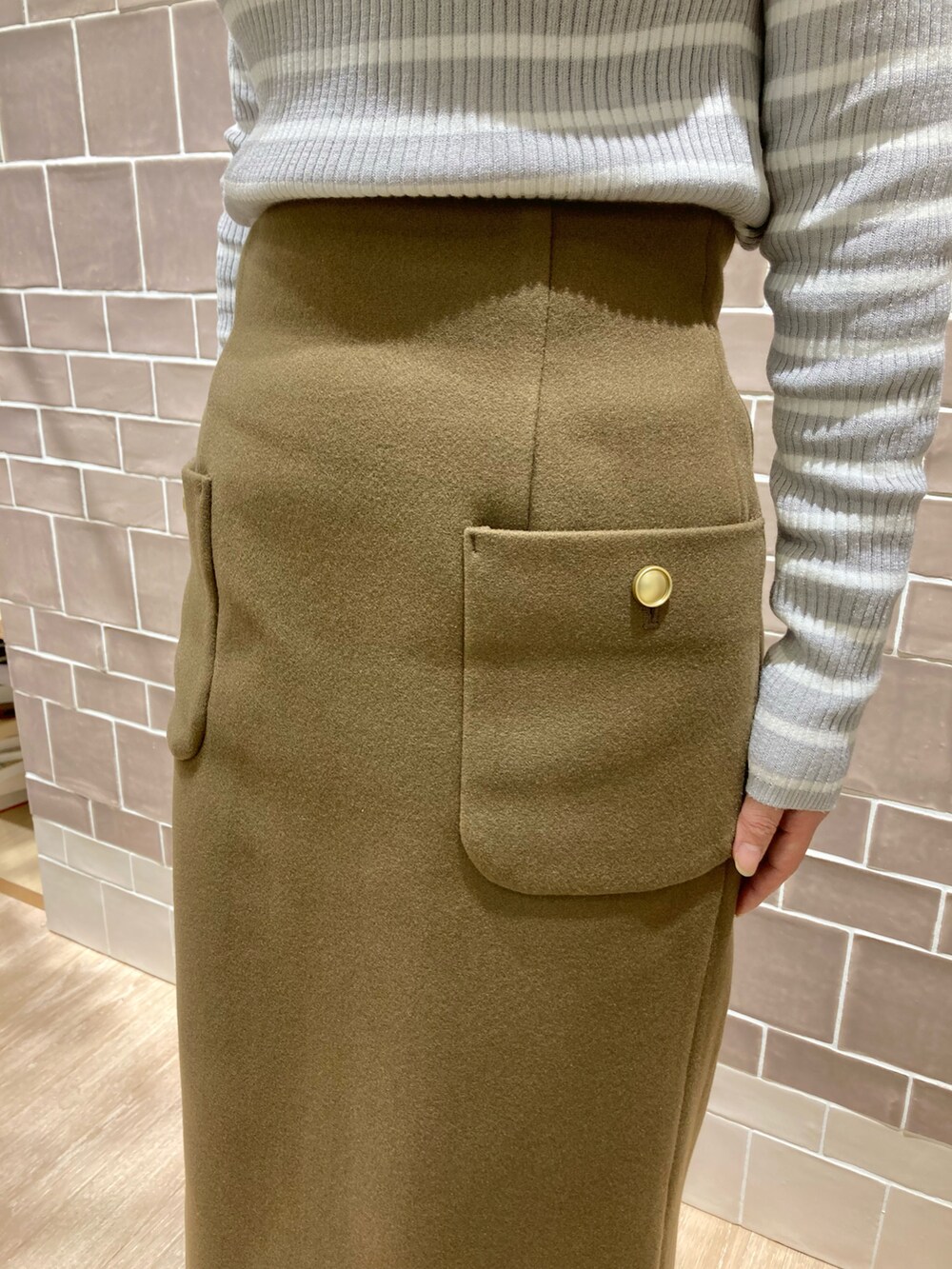 ブラウン系のスカート、グレー系のニット/セーター、ブラック系のブーツを着用したレディースの冬コーディネートの2枚目の写真