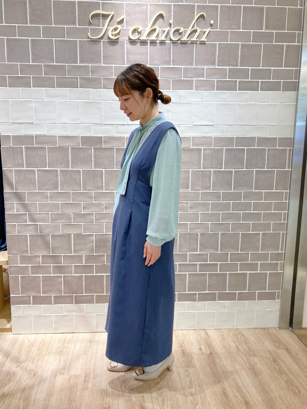 グリーン系のシャツ/ブラウス、ブルー系のジャンパースカート、ベージュ系のドレスシューズを着用したレディースの春コーディネートの2枚目の写真