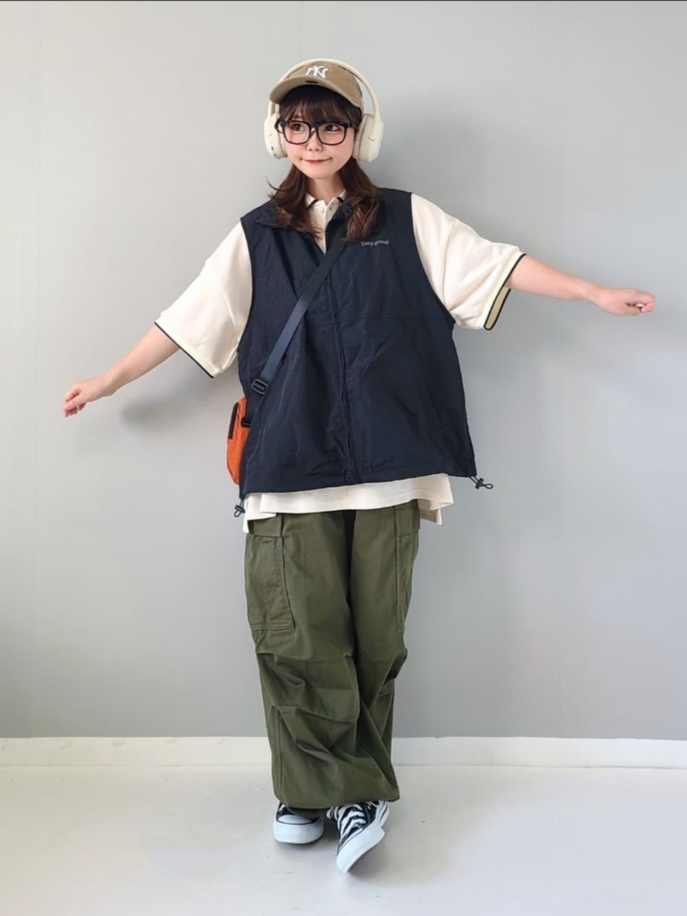 ブラック系のベスト、ホワイト系のポロシャツ、オレンジ系のショルダーバッグを着用したレディースの夏コーディネートの2枚目の写真