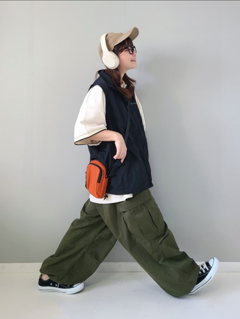 ブラック系のベスト、ホワイト系のポロシャツ、オレンジ系のショルダーバッグを着用したレディースの夏コーディネートの3枚目の写真