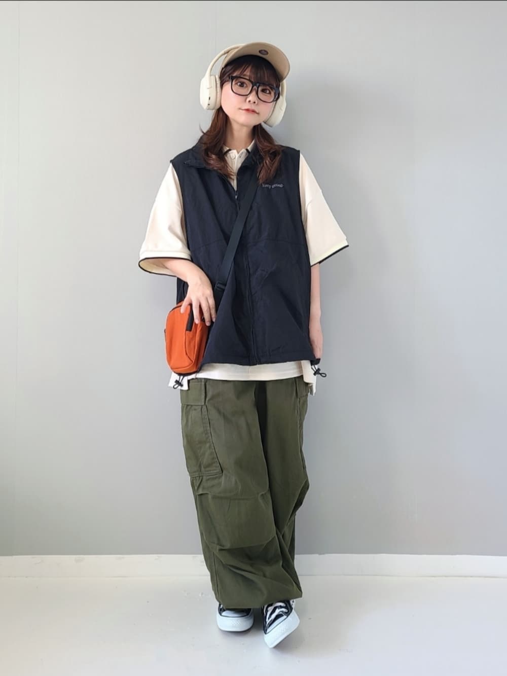 ブラック系のベスト、ホワイト系のポロシャツ、オレンジ系のショルダーバッグを着用したレディースの夏コーディネートの5枚目の写真