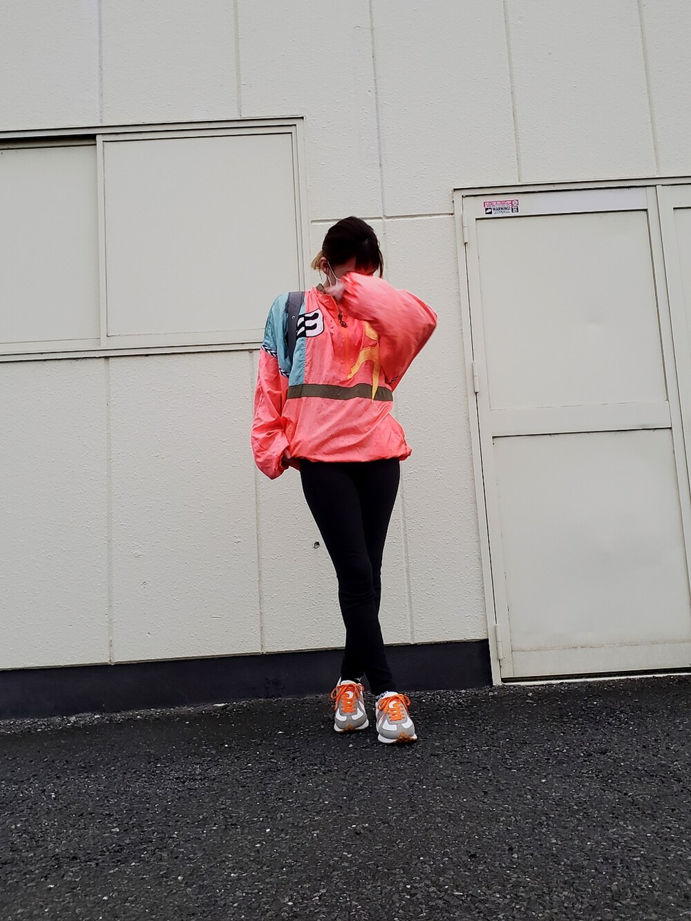 オレンジ系のナイロンジャケット、ブラック系のパンツを着用したレディースの夏コーディネートの2枚目の写真