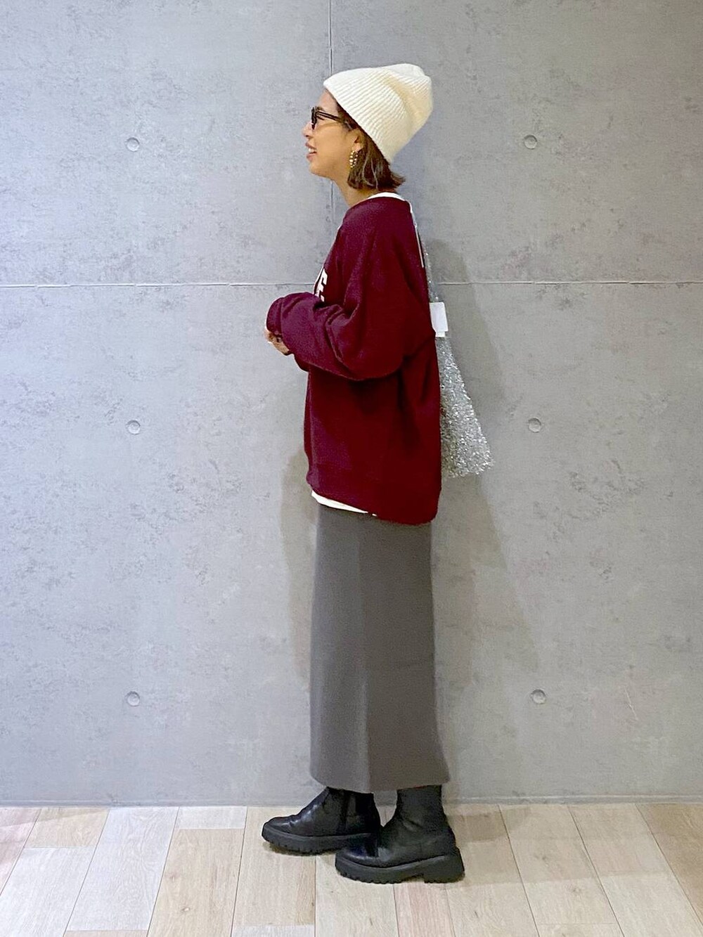 グレー系のスカート、ブラック系のブーツ、レッド系のスウェットを着用したレディースの秋コーディネートの2枚目の写真