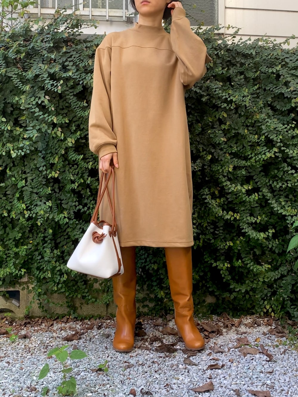 ベージュ系のワンピース、ブラウン系のブーツ、ホワイト系のハンドバッグを着用したレディースの秋コーディネートの2枚目の写真