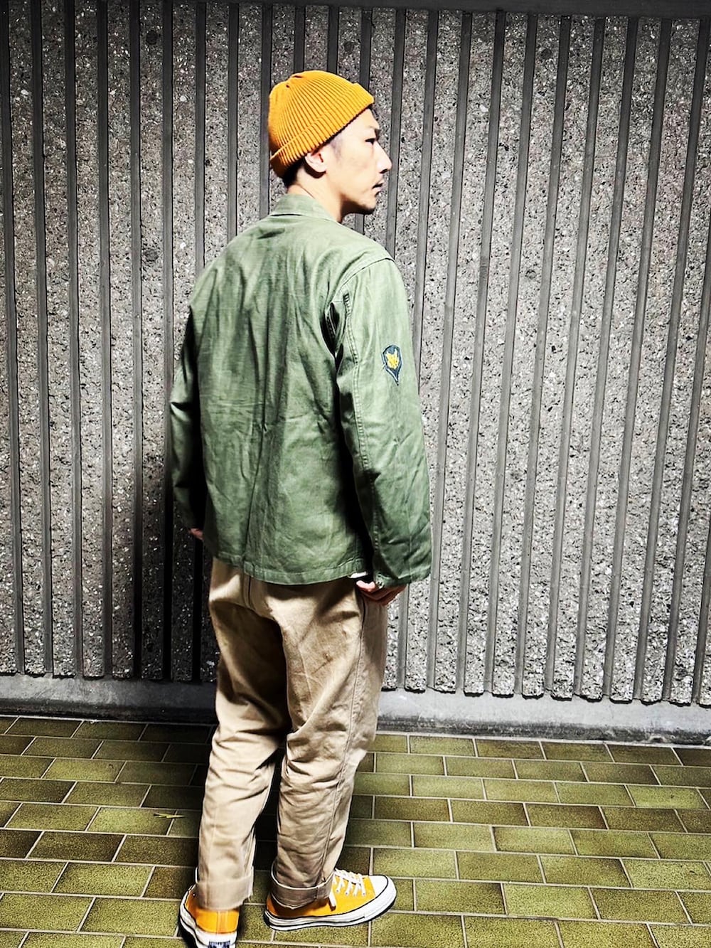 グリーン系のミリタリージャケット、ホワイト系のトップス、グリーン系のチノパンツを着用したメンズの秋コーディネートの3枚目の写真