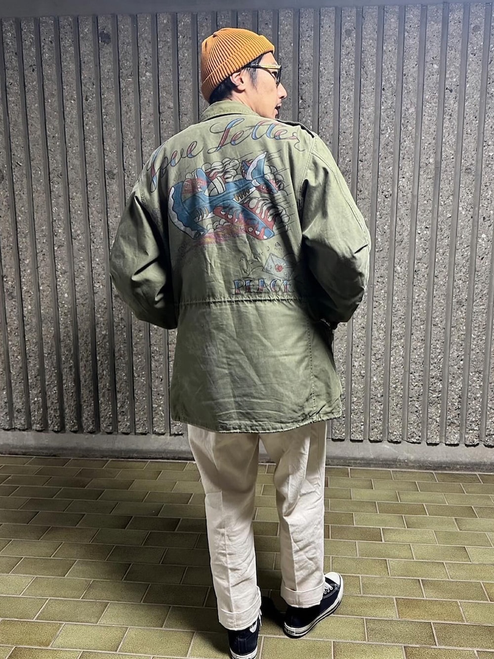 グリーン系のミリタリージャケット、ベージュ系のチノパンツ、ブラック系のスニーカーを着用したメンズの冬コーディネートの3枚目の写真