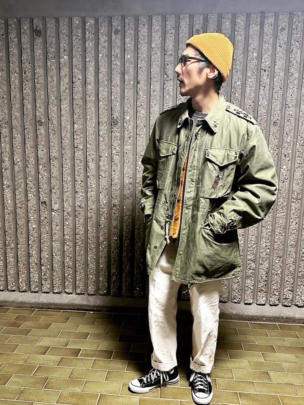 グリーン系のミリタリージャケット、ベージュ系のチノパンツ、ブラック系のスニーカーを着用したメンズの冬コーディネートの2枚目の写真