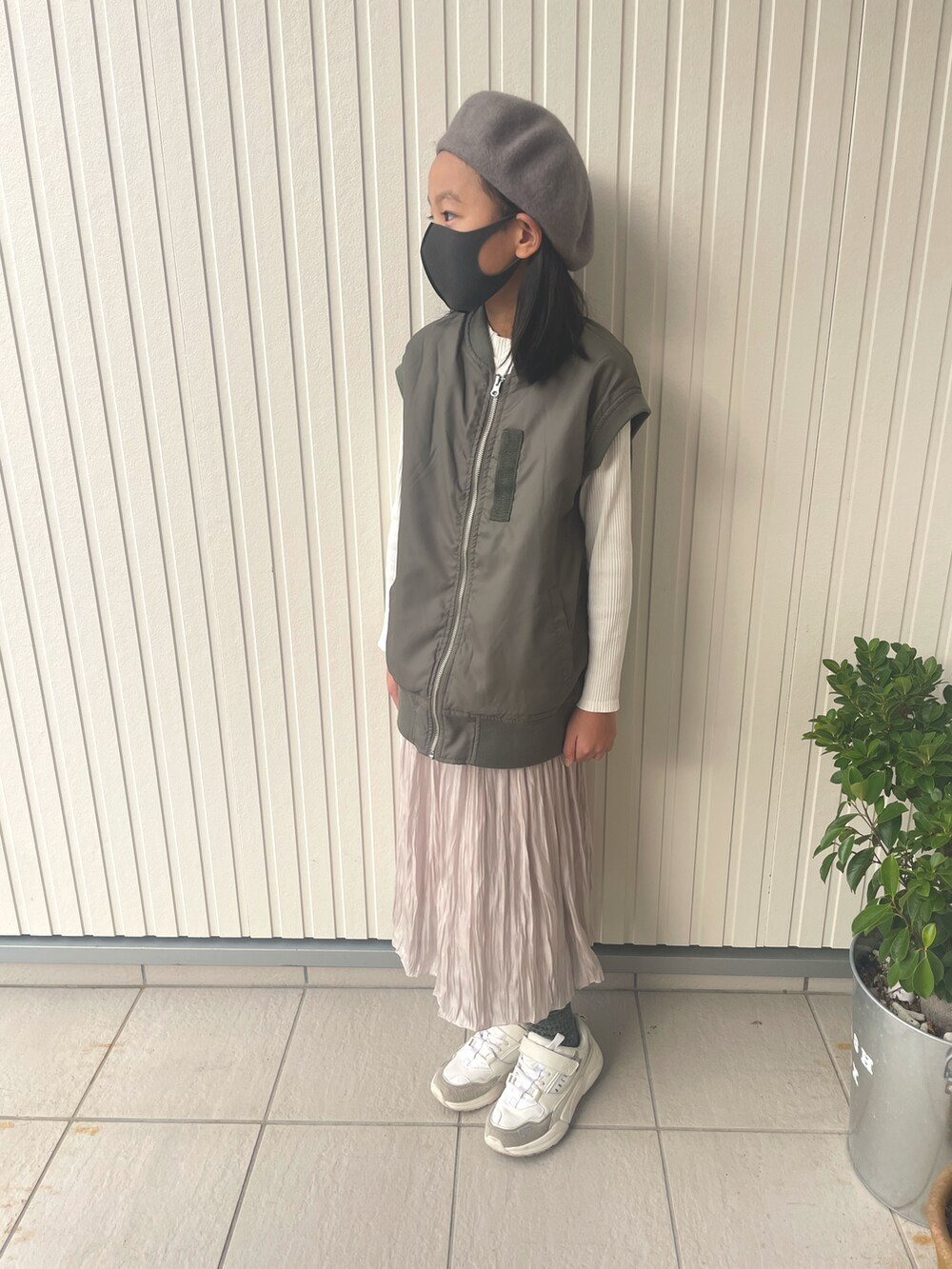 ホワイト系のトップス、グリーン系のダウンベスト、ホワイト系のスカートを着用したキッズの冬コーディネートの2枚目の写真