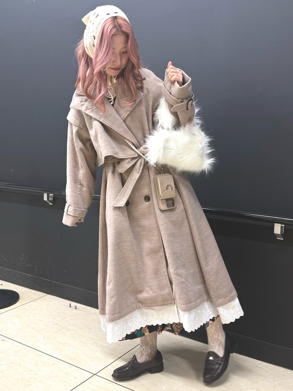 ベージュ系のチェスターコート、ブラウン系のローファー、ホワイト系のハンドバッグを着用したレディースの冬コーディネートの2枚目の写真