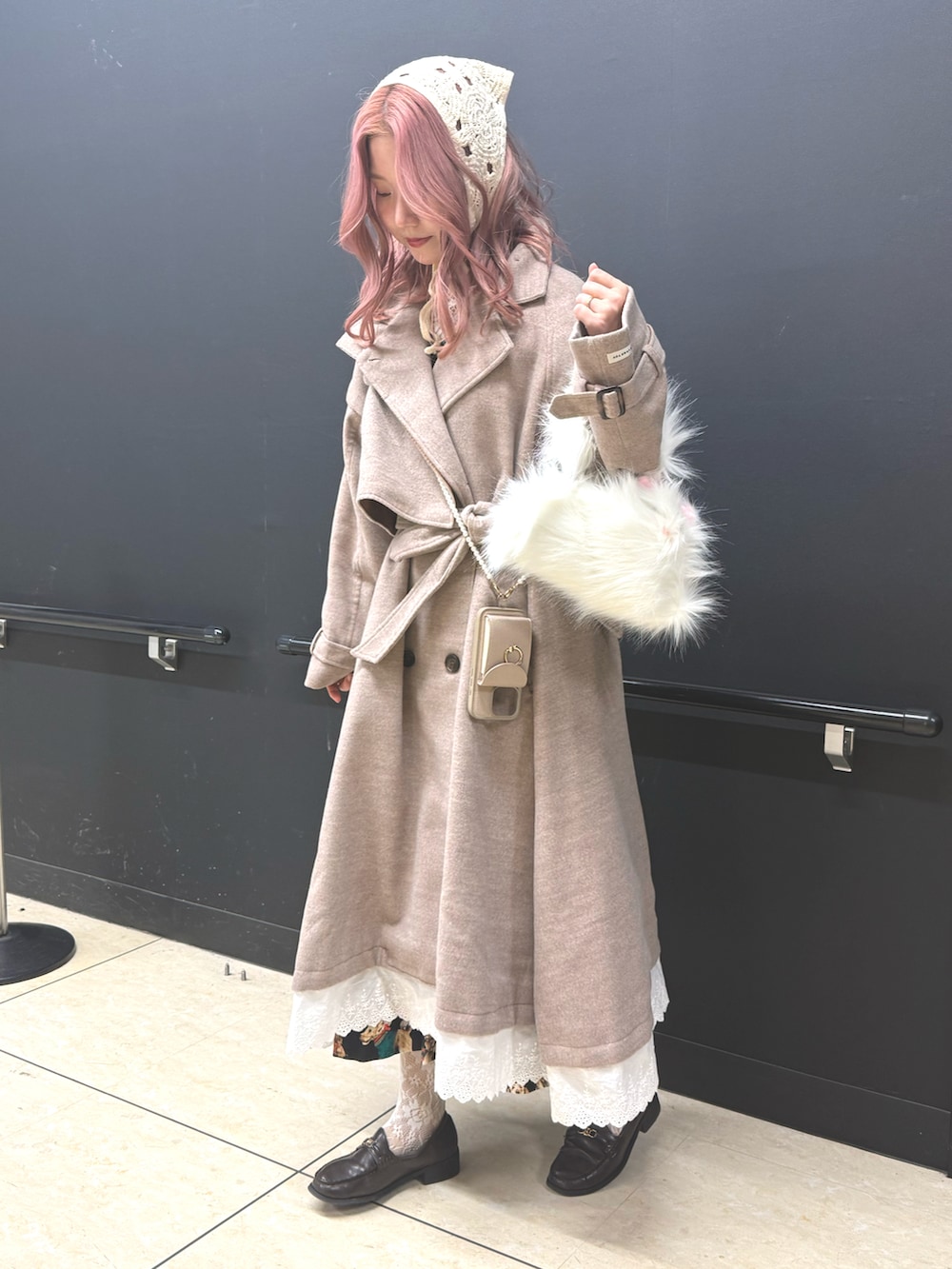 ベージュ系のチェスターコート、ブラウン系のローファー、ホワイト系のハンドバッグを着用したレディースの冬コーディネートの3枚目の写真